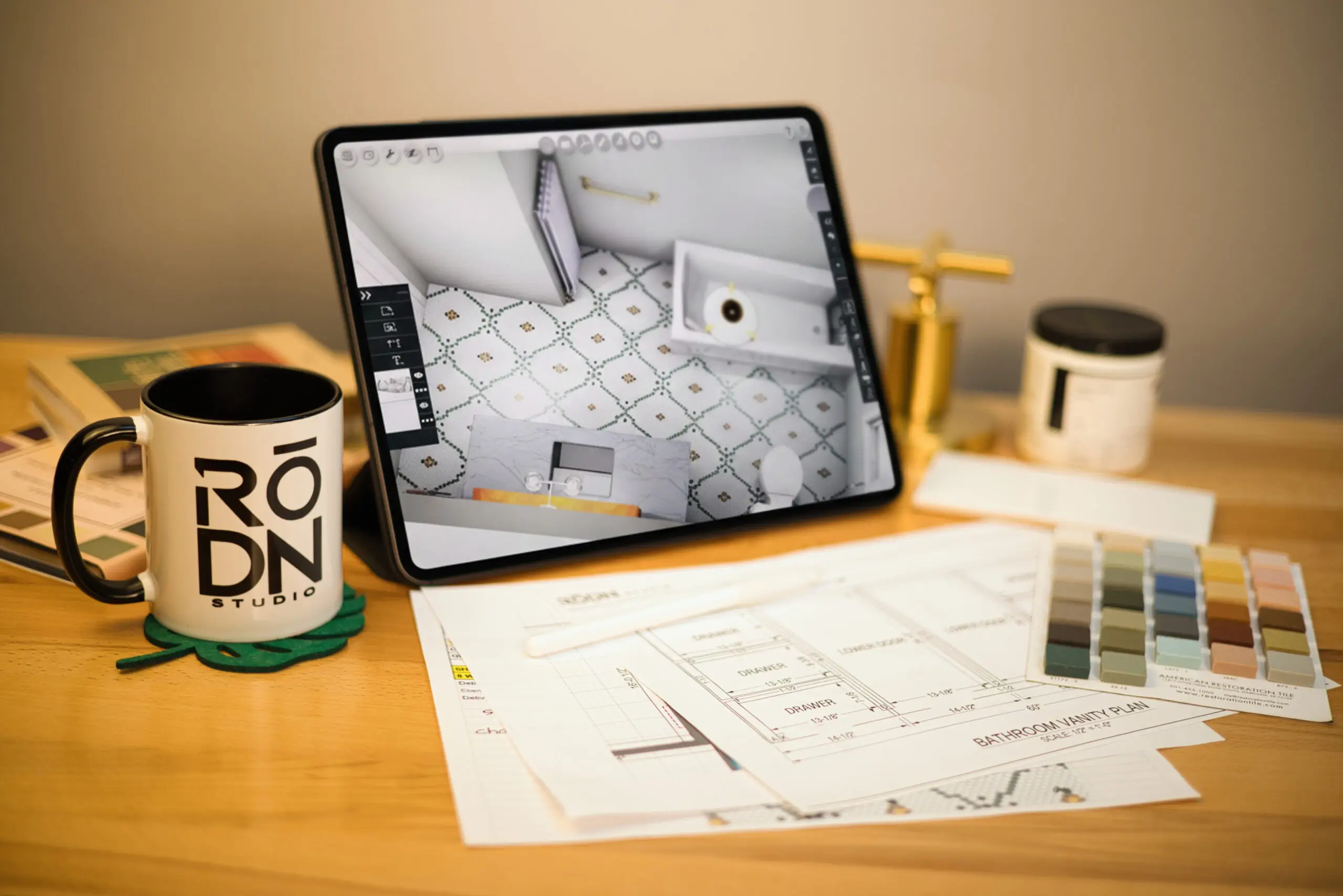 An iPad displaying a bathroom design, with drawings and material samples on the studio table